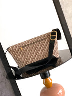 Dior bag side view with beige monogram canvas, black strap, gold-toned buckle hardware.