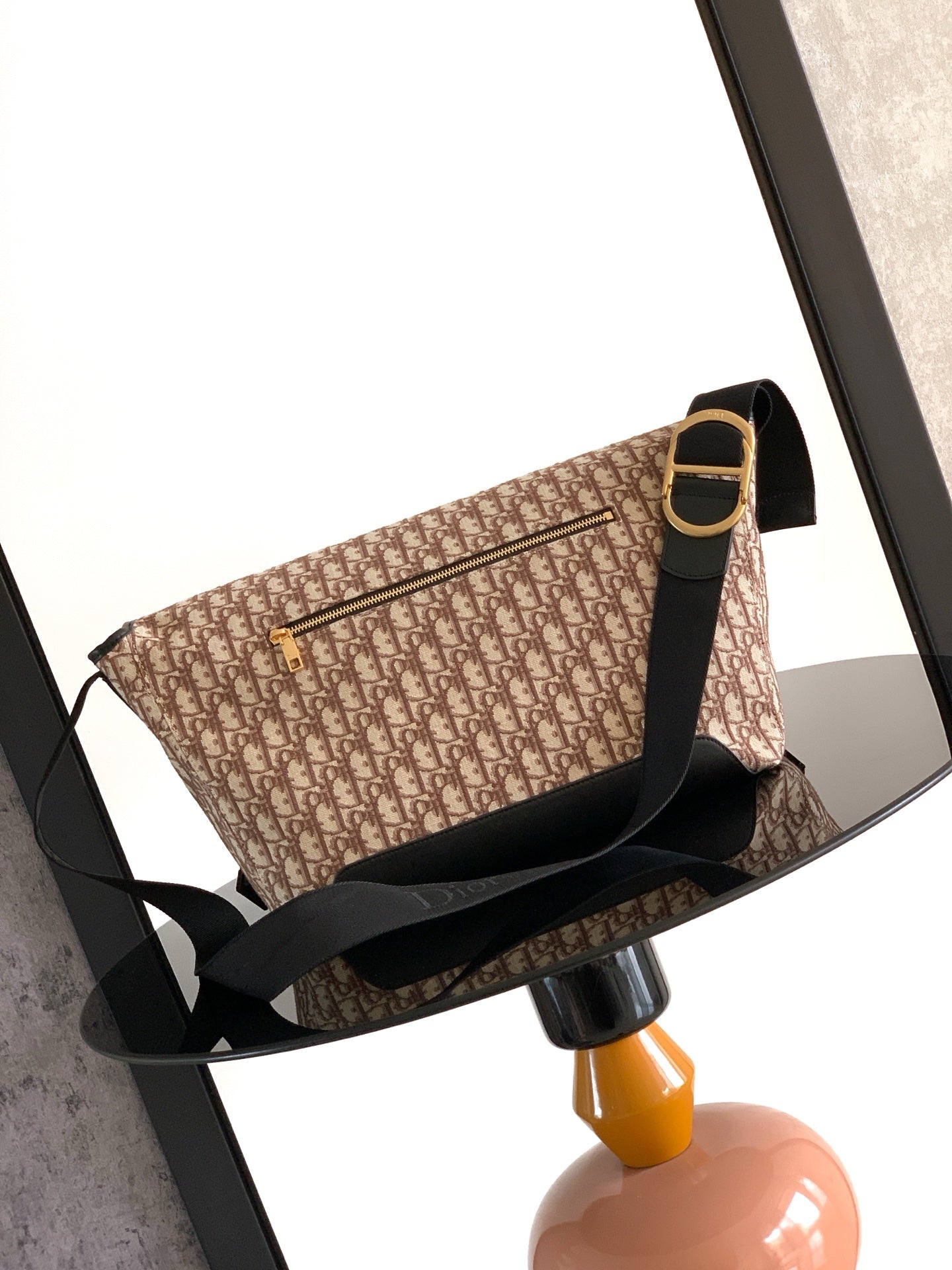 Dior bag side view with beige monogram canvas, black strap, gold-toned buckle hardware.