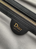 Dior bag zipper close-up with gold teeth on black leather, Dior logo on tab.