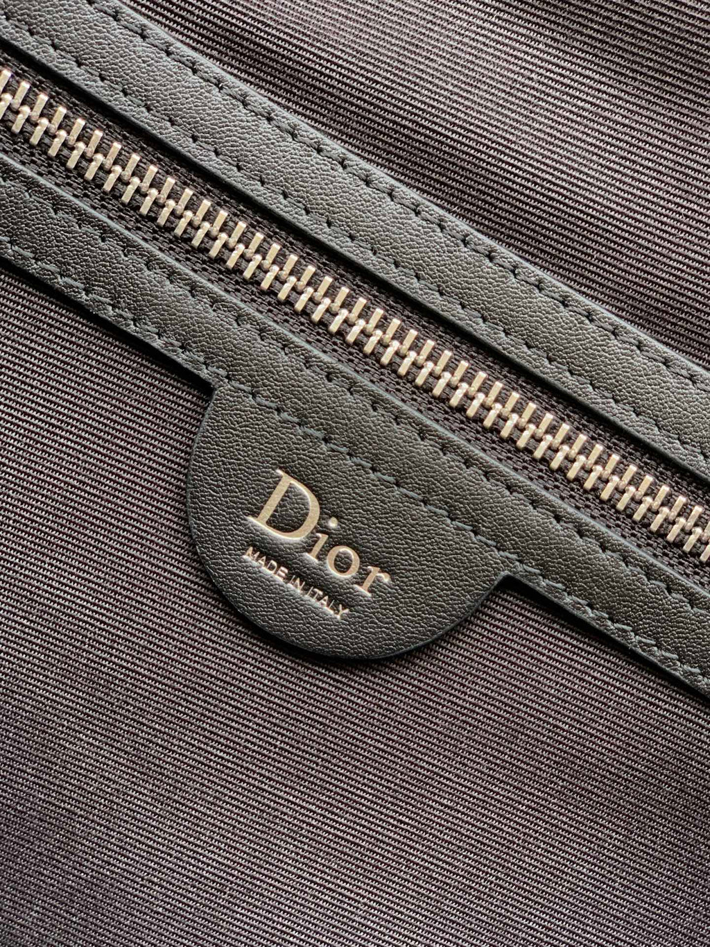 Dior zipper pull and leather pocket on dark fabric bag front