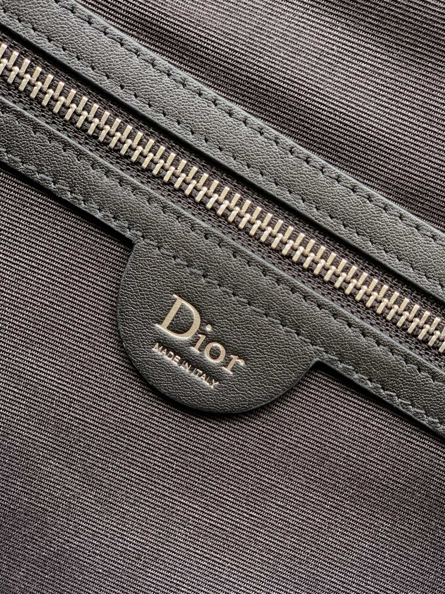 Dior zipper pull and leather pocket on dark fabric bag front