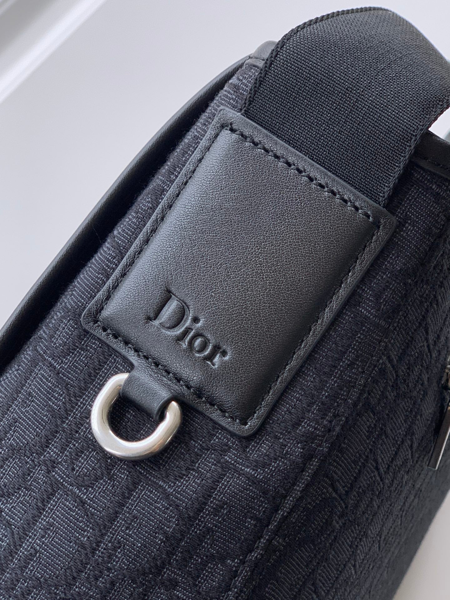 Dior logo leather tab with stitching on dark woven bag strap