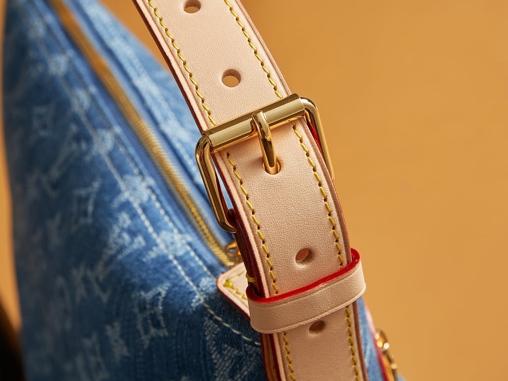 Tan leather strap attachment with gold-tone buckle on blue denim handbag