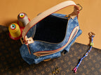 Blue denim handbag open top with monogram lining, tan trim, and gold zipper hardware