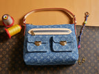 Blue denim handbag with monogram print, tan top handles, and gold-tone hardware