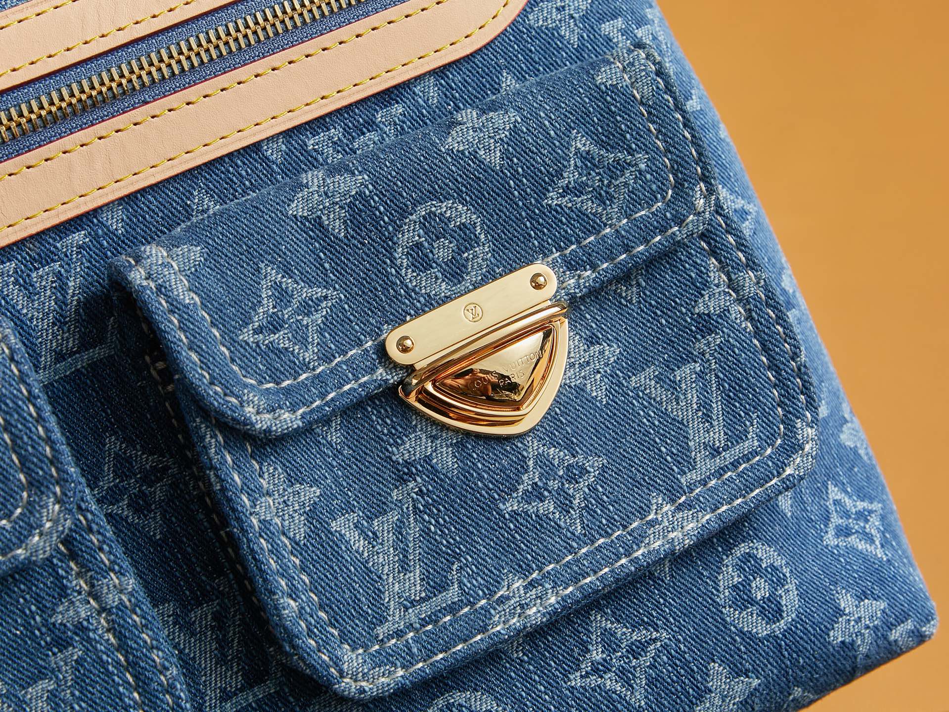 Blue denim flap pocket detail with monogram stitching and gold-tone clasp