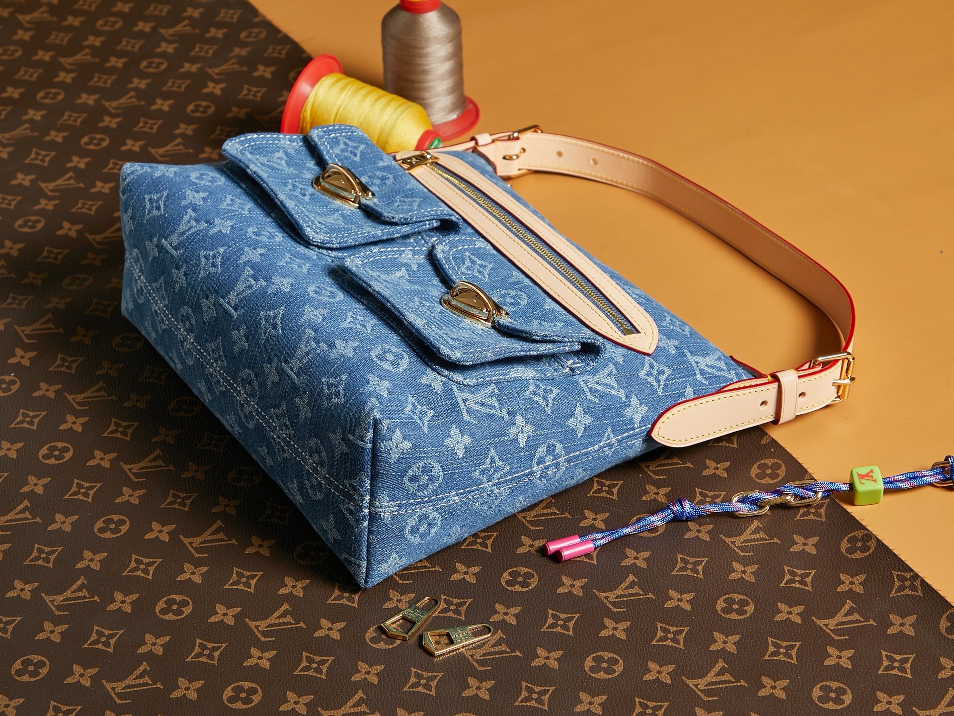 Blue denim handbag with monogram print, tan strap and top handle, gold-tone buckles