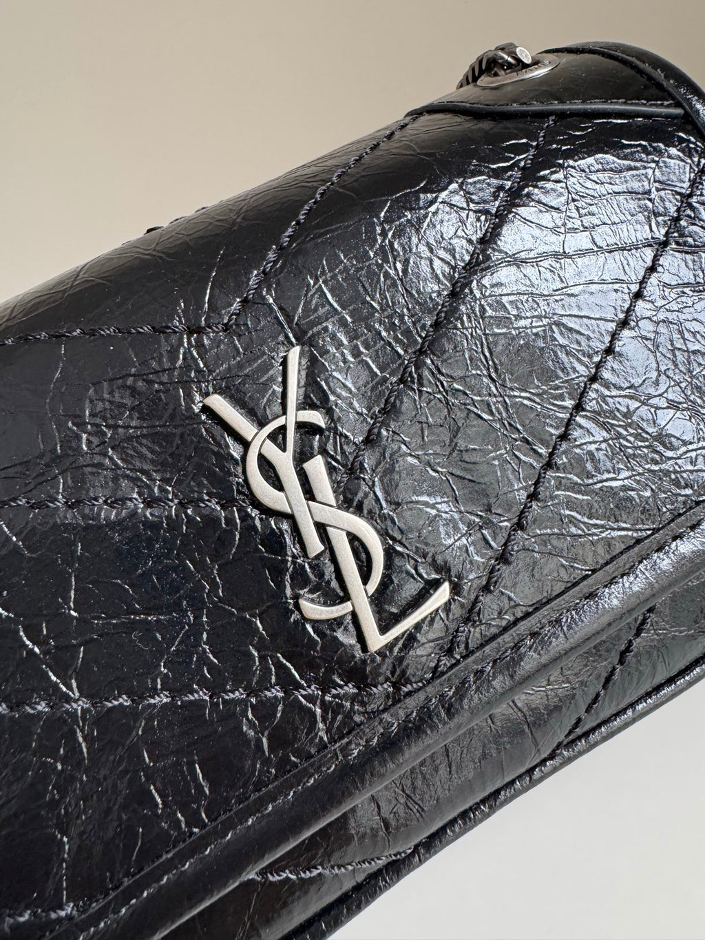 Black leather flap close-up with YSL metal logo and stitched border