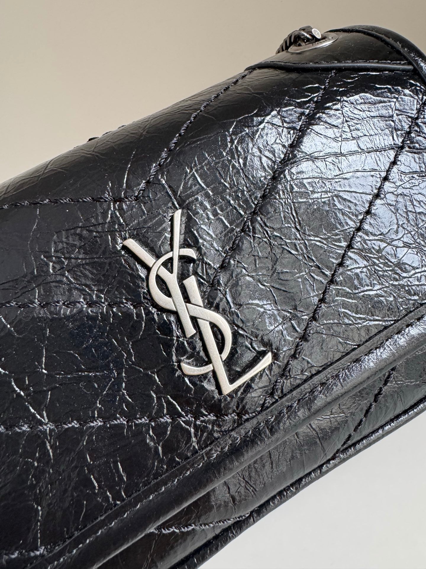 Black leather flap close-up with YSL metal logo and stitched border