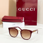 Sunglasses with burgundy frames and brown tinted lenses, gold logo temple details