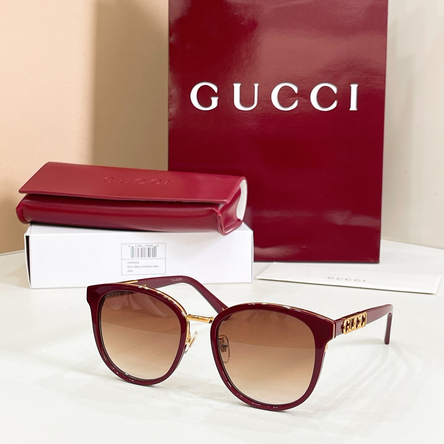 Sunglasses with burgundy frames and brown tinted lenses, gold logo temple details