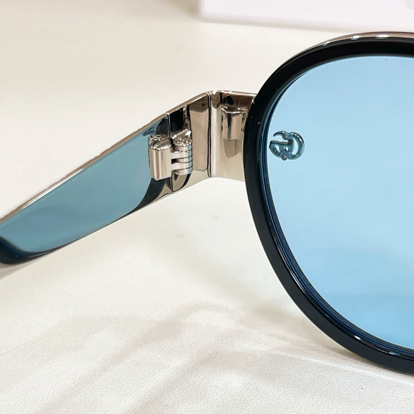 Round sunglasses close-up: dark rim with metallic hinge and blue temple arm