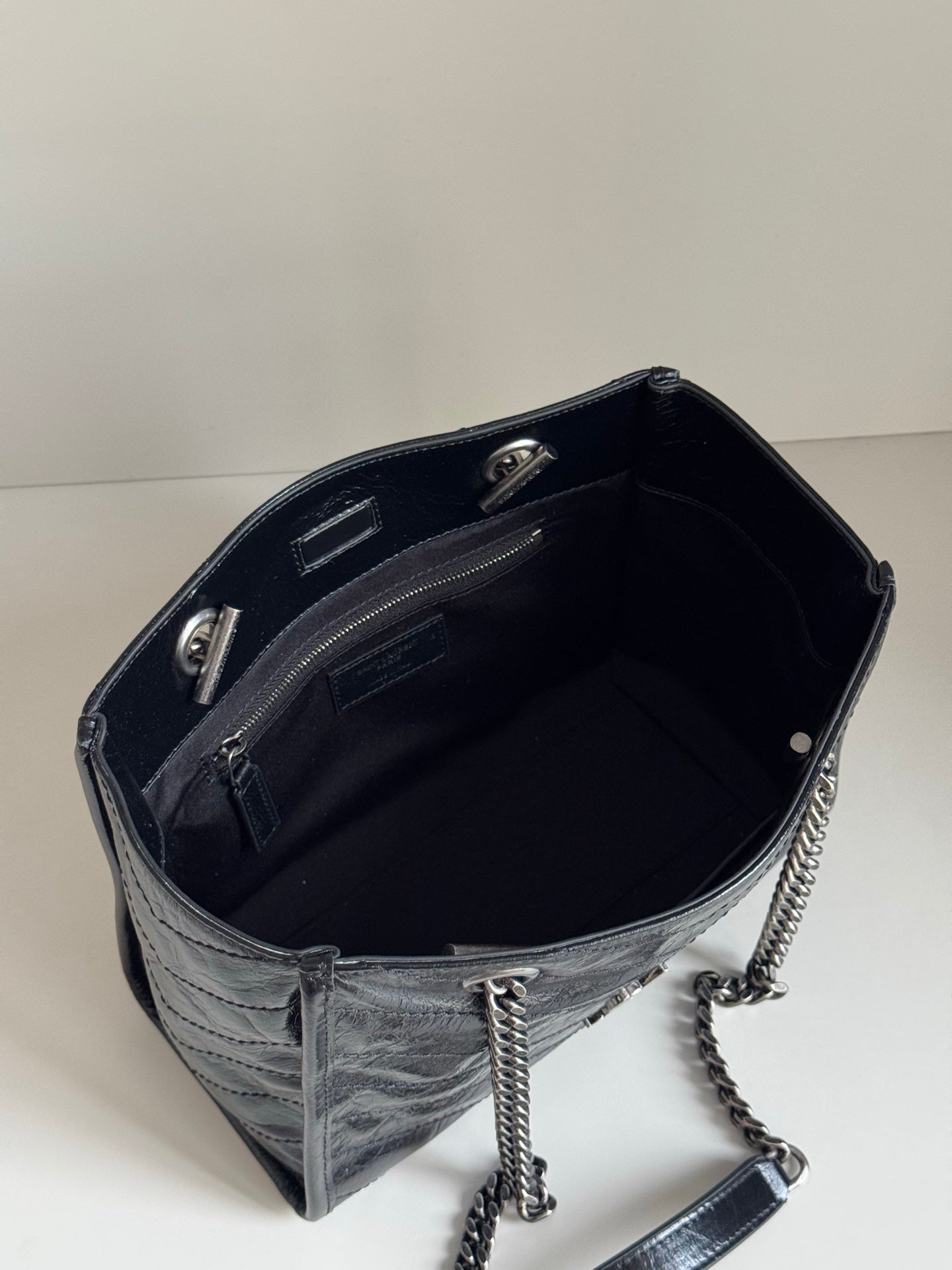Dark leather tote bag interior view with zip pocket and chain strap