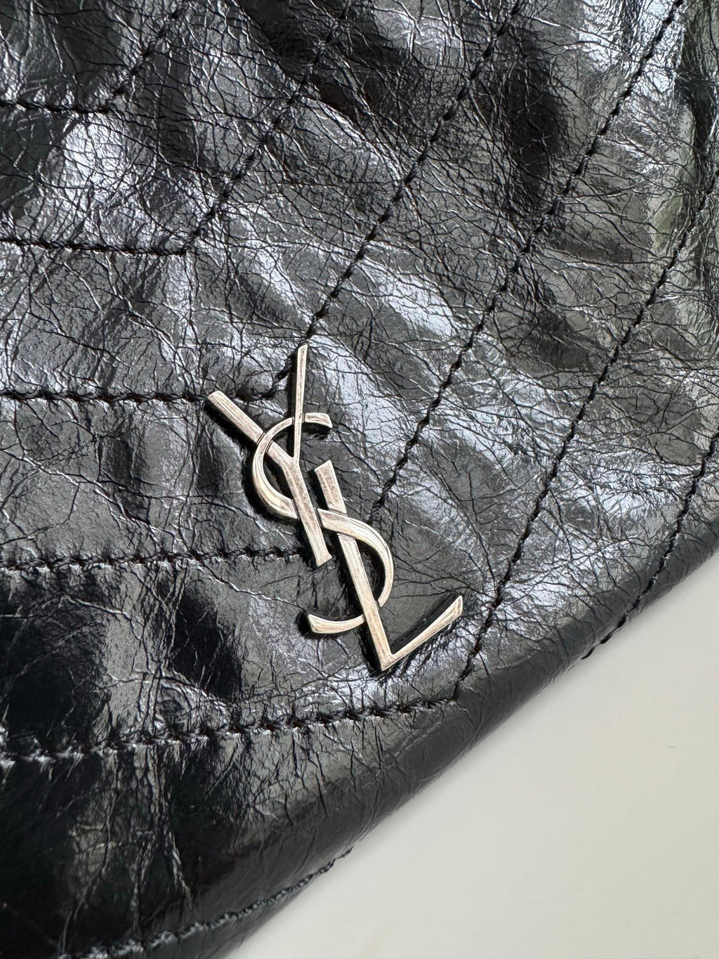 Dark leather tote bag close-up of YSL monogram charm on the front