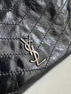 Dark leather tote bag close-up of YSL monogram charm on the front