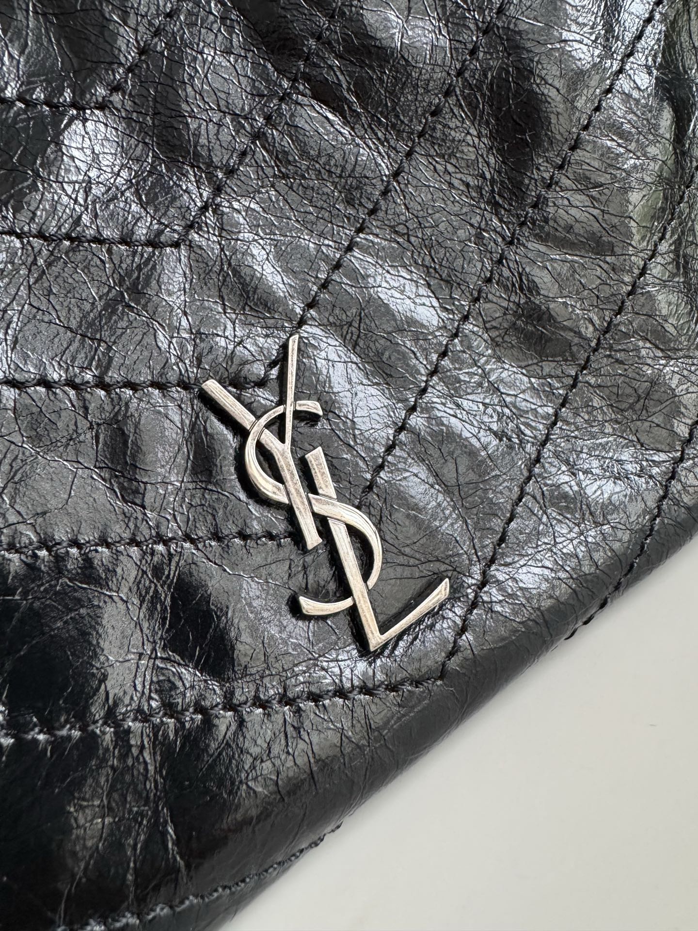 Dark leather tote bag close-up of YSL monogram charm on the front
