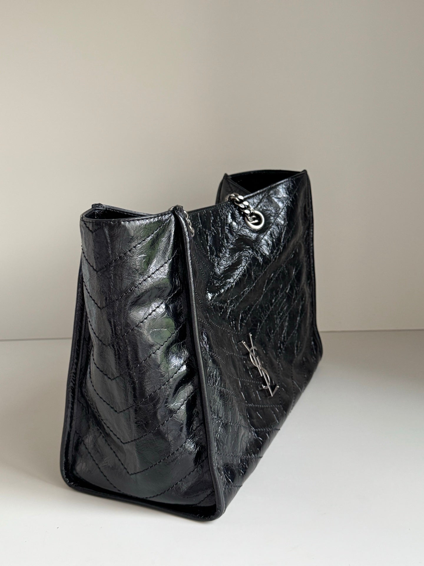 Black leather tote bag side view with textured finish and chain strap