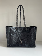 Black leather tote bag with chain handles and YSL logo on front