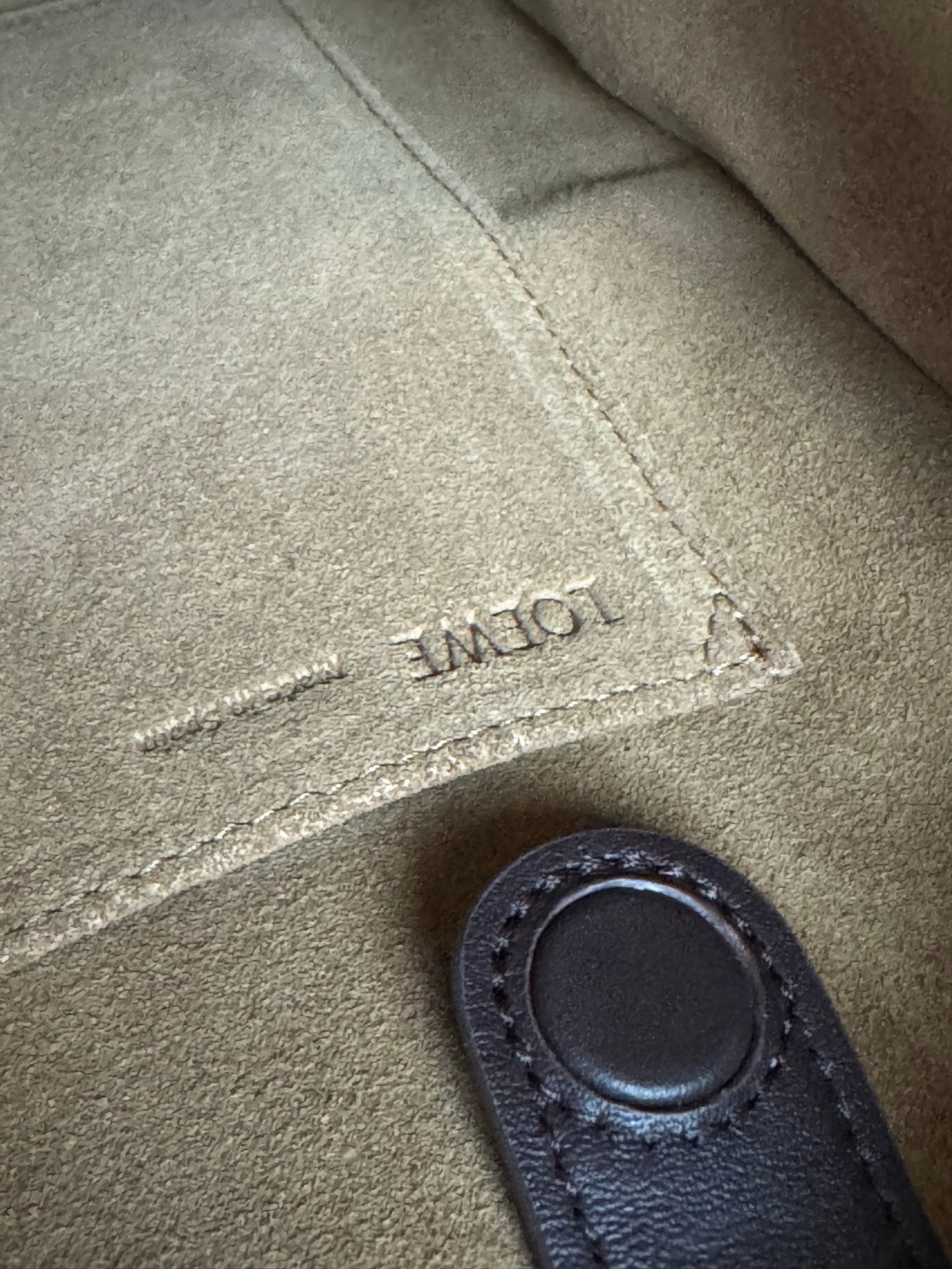 Loewe leather close-up with engraved logo text and stitched dark leather handle tab
