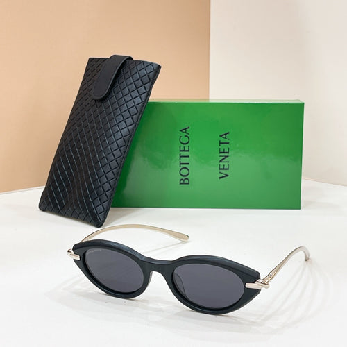 Black sunglasses with dark lenses, gold-toned hinges, beside textured black case.