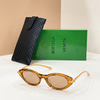 Amber sunglasses with amber lenses and gold-toned frame accents, beside textured black case.