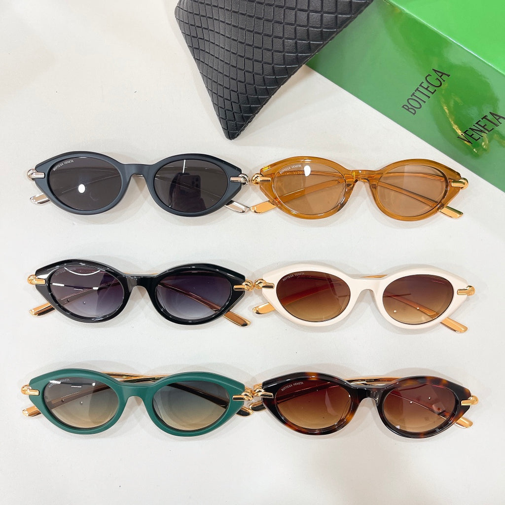 Assorted sunglasses: black, amber, cream, and green frames with gold hinges, beside case.