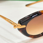 Tortoiseshell sunglasses close-up with gold hinge and brown-tinted lens.