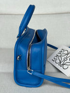 Blue leather mini bag standing with two zippers and shoulder strap; keyring detail