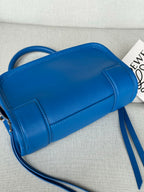 Blue leather mini cylinder bag with structured front panel and adjustable shoulder strap