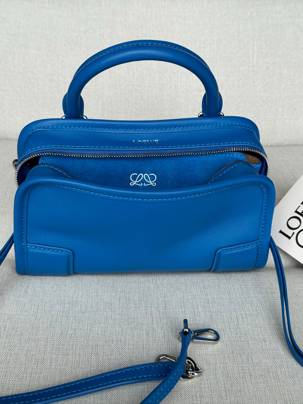 Blue leather handbag with top handle, front logo detail, and two zip compartments
