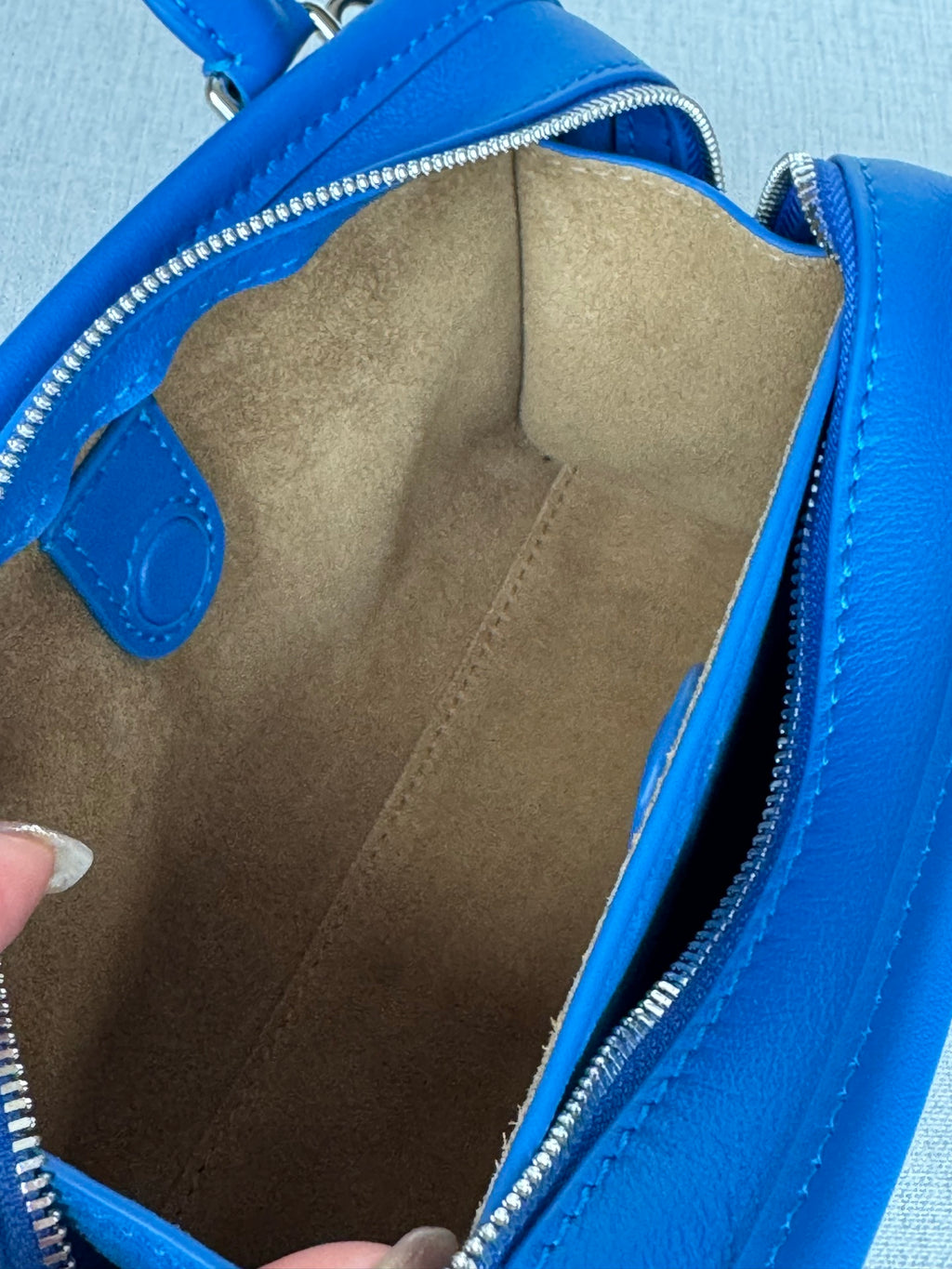 Opened blue leather bag showing beige suede-like interior lining and zipper track