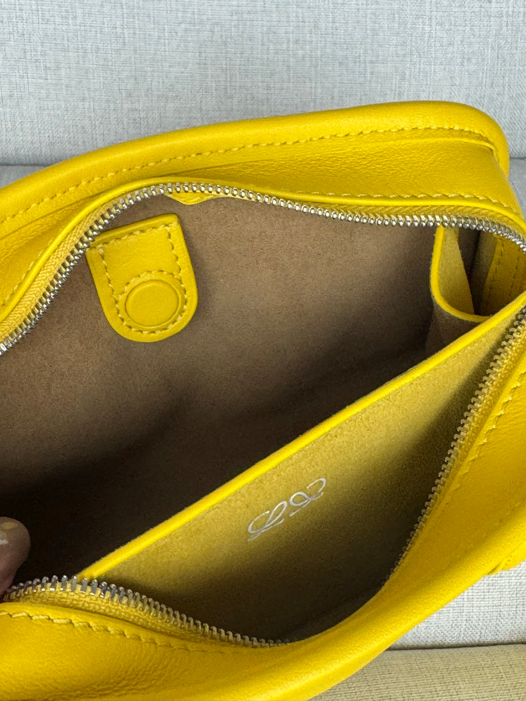 Close-up interior of yellow leather bag with zipper, logo, and pocket lining