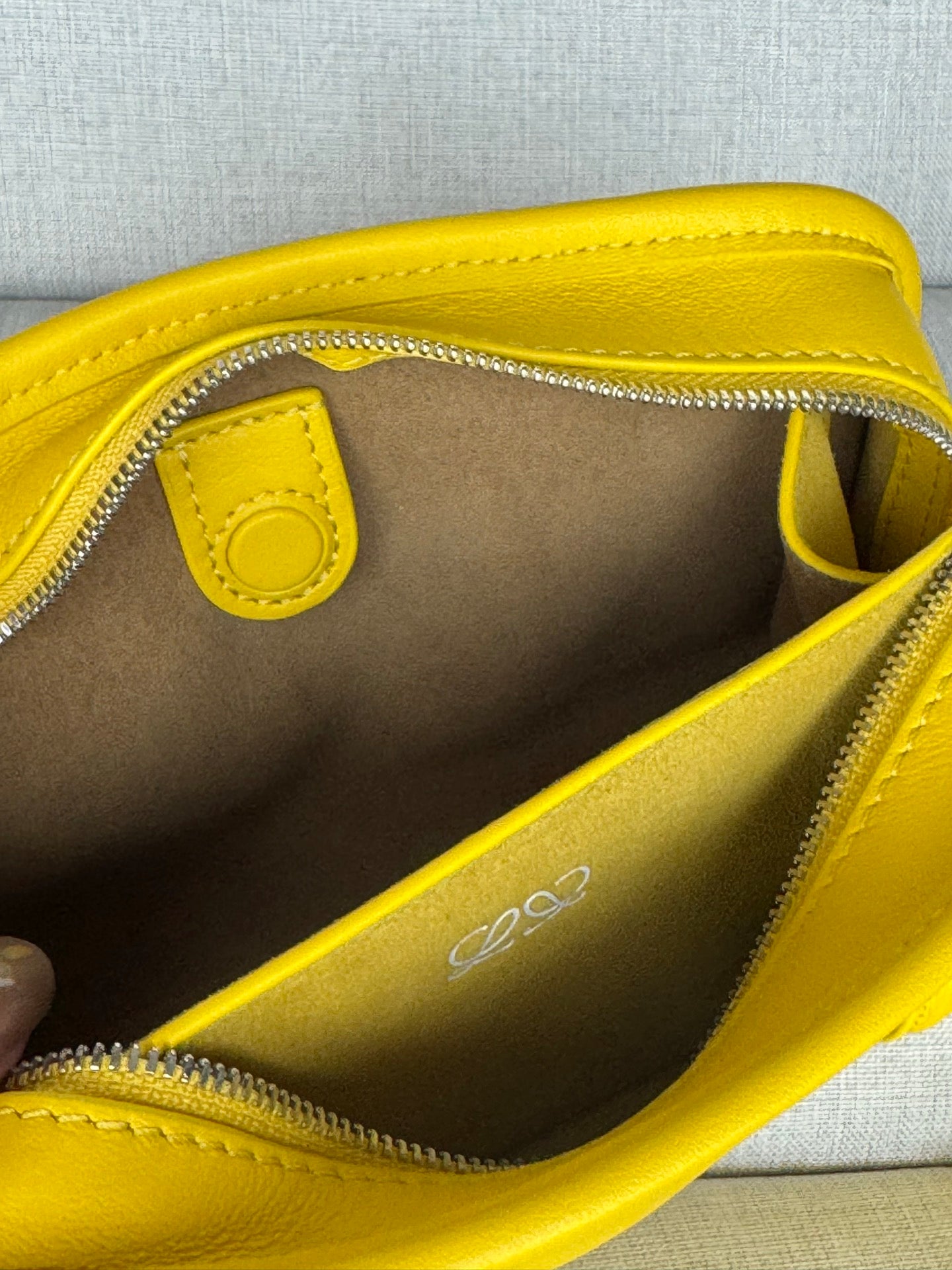 Close-up interior of yellow leather bag with zipper, logo, and pocket lining