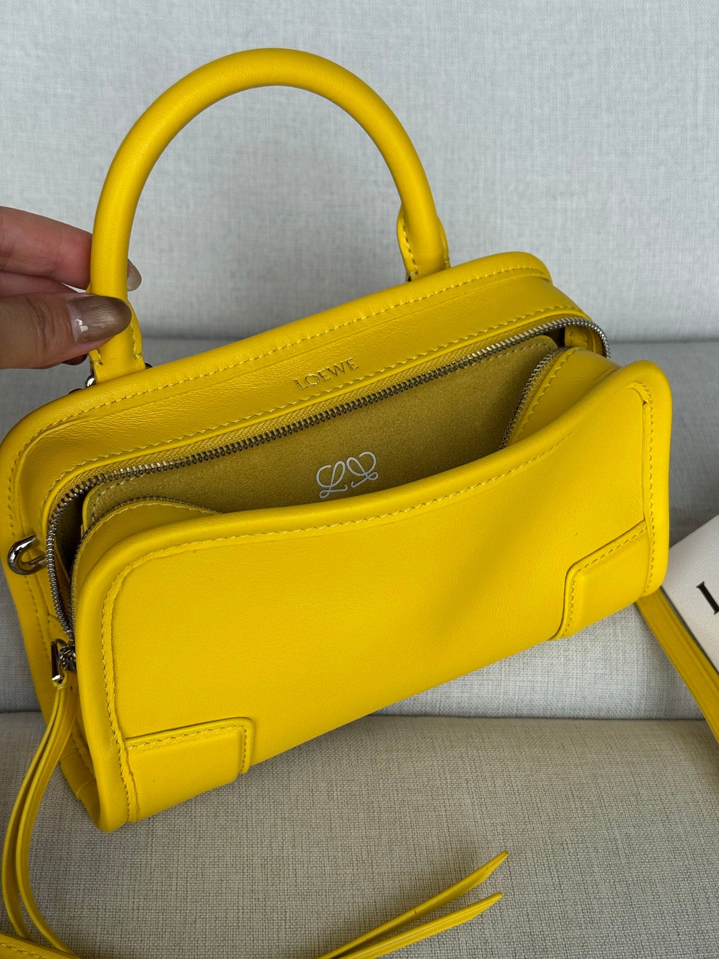 Yellow leather top-handle bag held open, showing zipper and logo patch