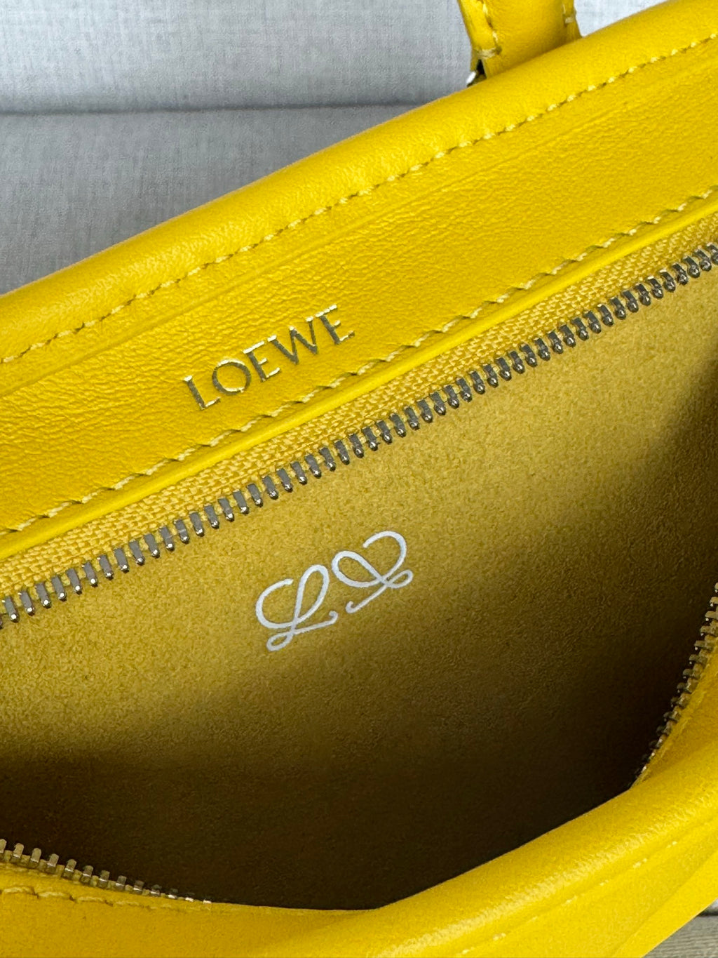 Close-up of yellow leather bag zipper trim with LOEWE logo and stitched edge