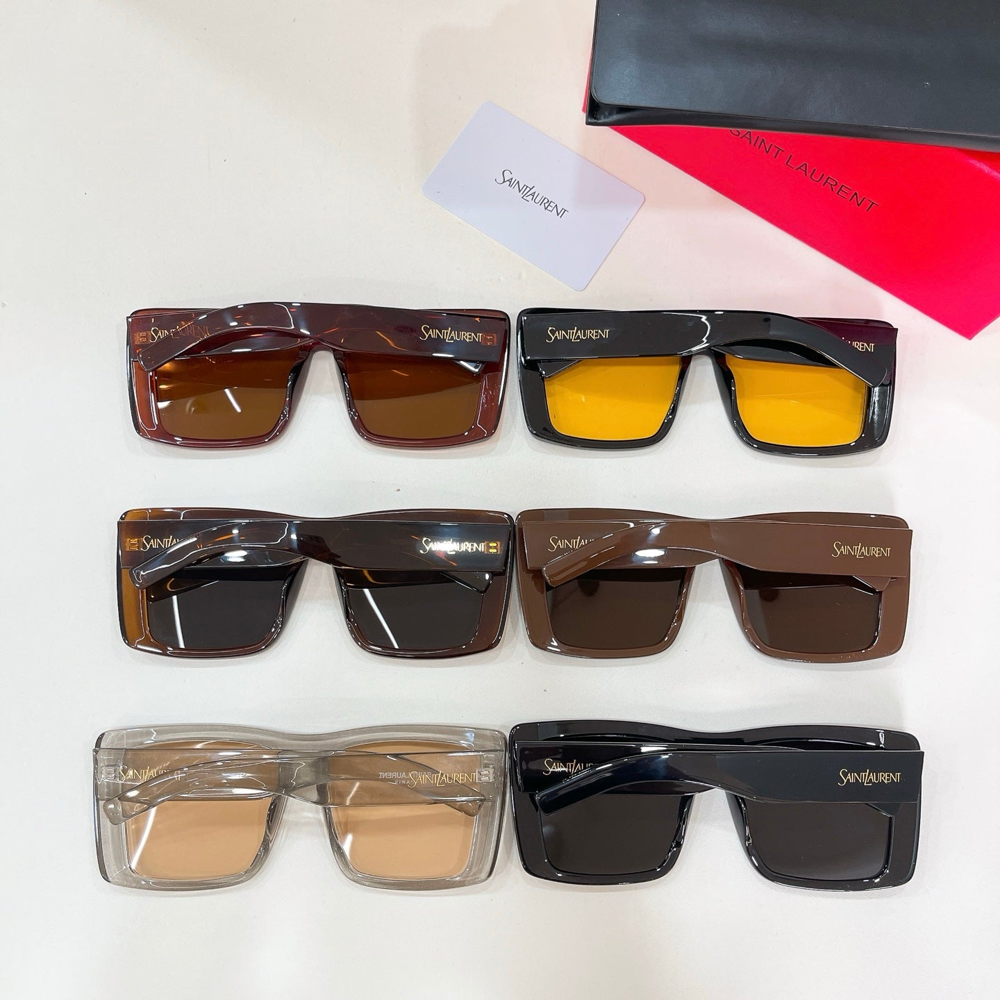 Display of multiple square sunglasses with dark and amber lenses, YSL logos.