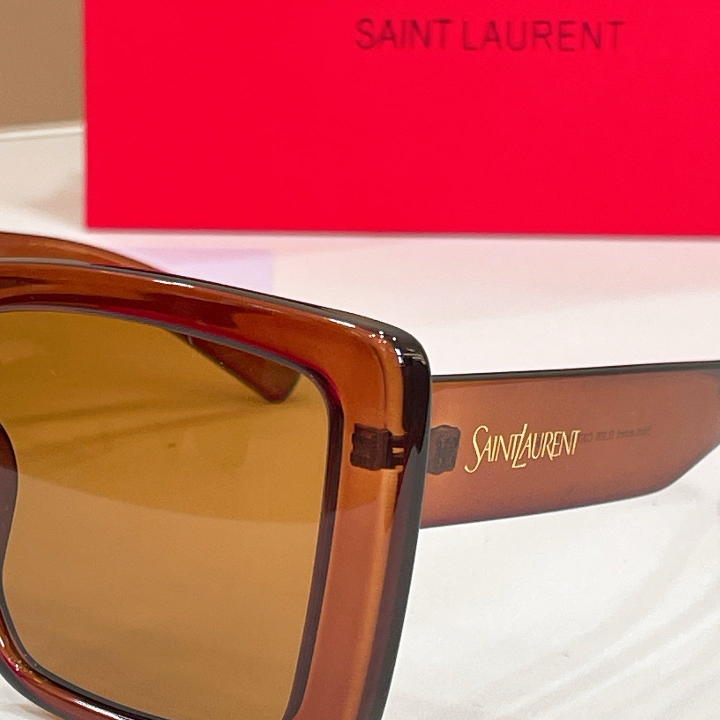 Rectangular brown sunglasses arm close-up with YSL branding and logo.