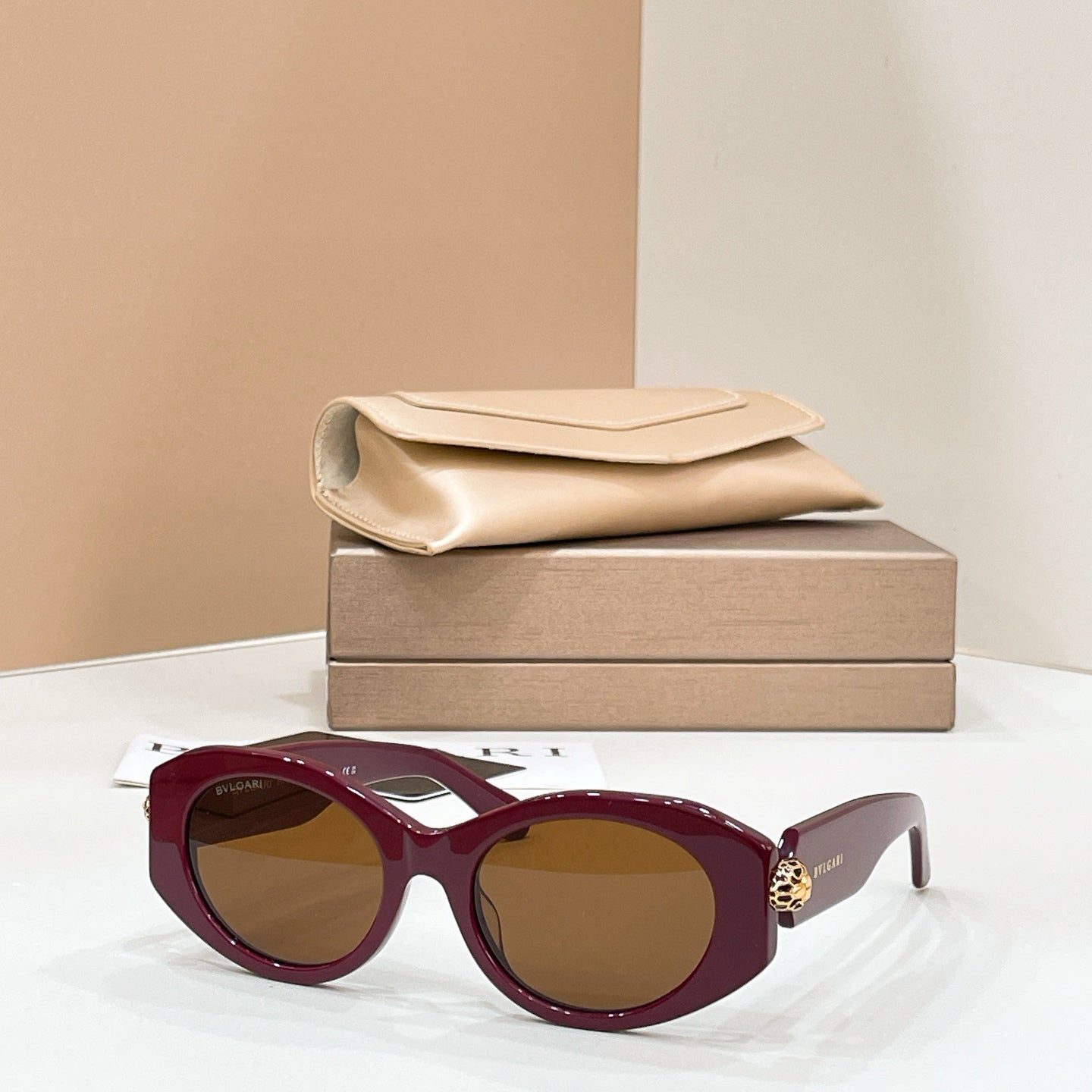 Bvlgari round sunglasses with burgundy frame and amber lenses, gold-toned charm on temple.