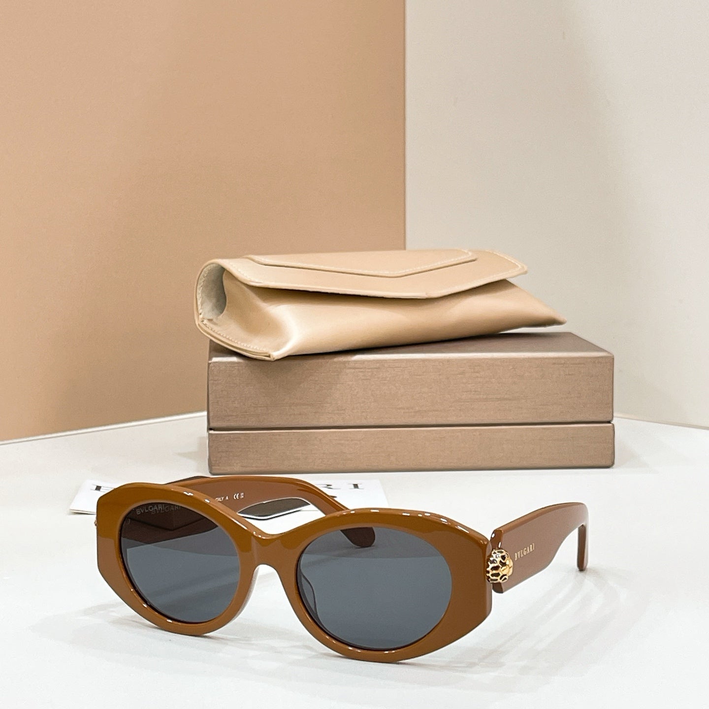 Bvlgari round sunglasses with brown frame and blue-tinted lenses, gold-toned charm on temple.