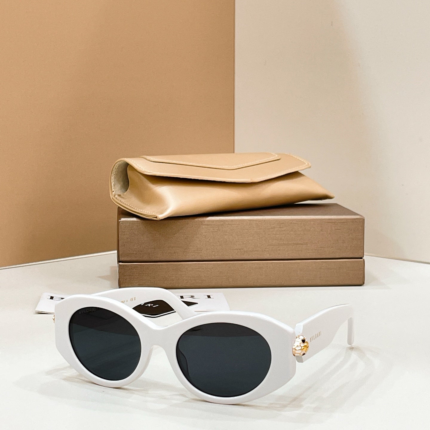 Bvlgari round sunglasses with white frame and dark lenses, gold-toned charm on temple.