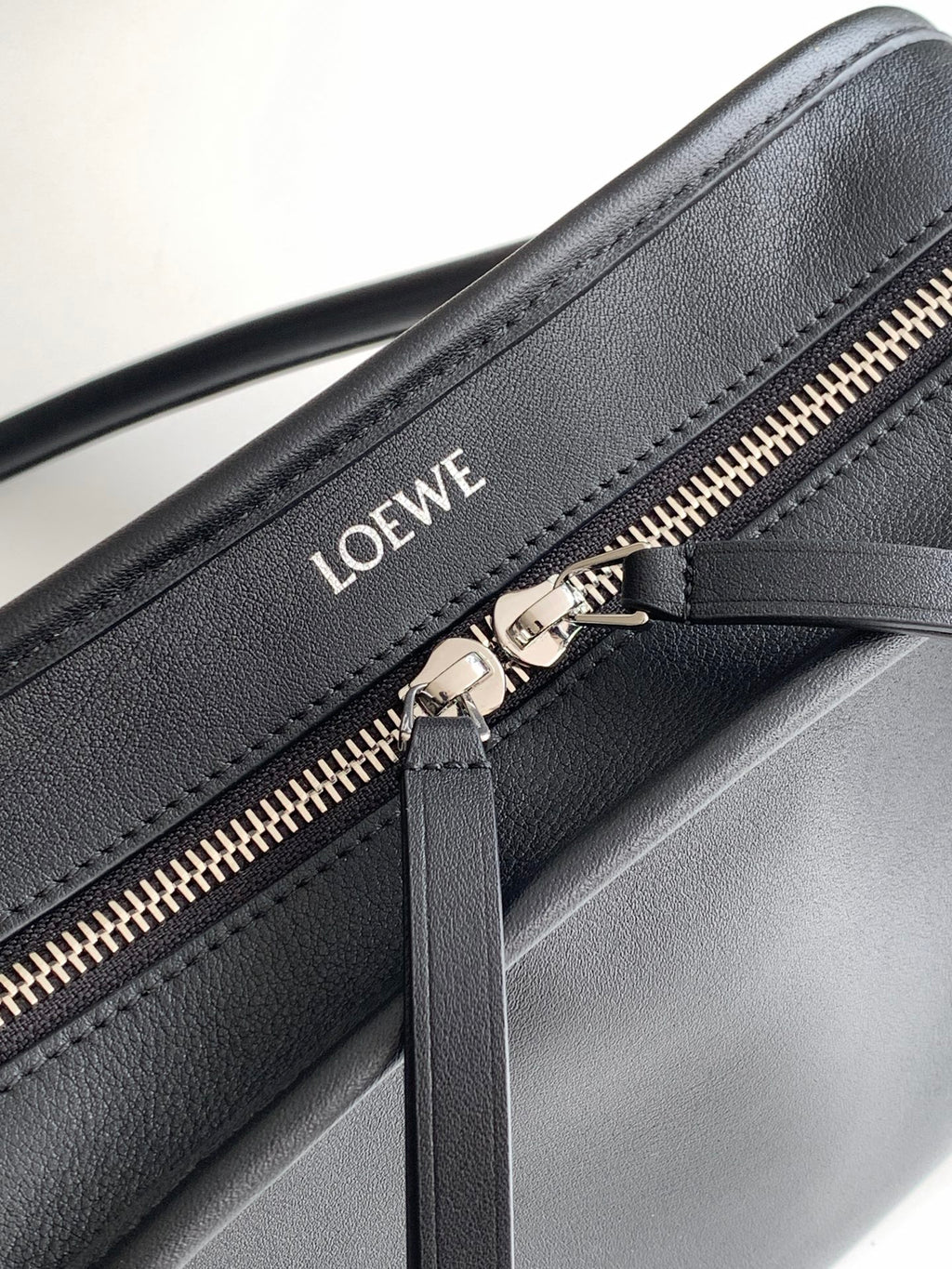 Black leather bag close-up: gold zipper and Loewe logo on front panel