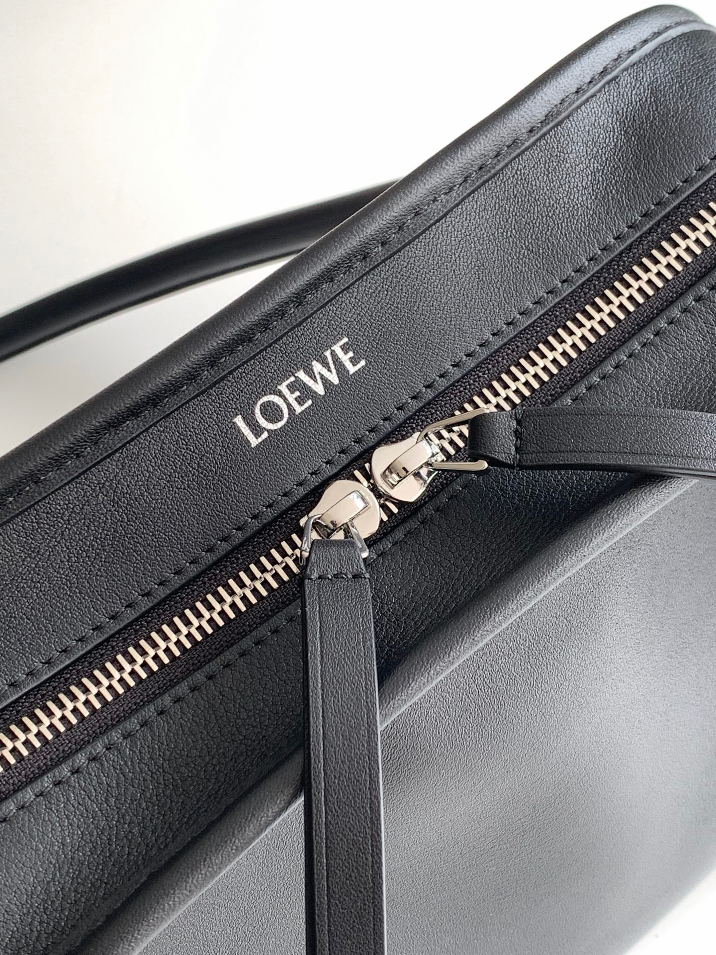 Black leather bag close-up: gold zipper and Loewe logo on front panel