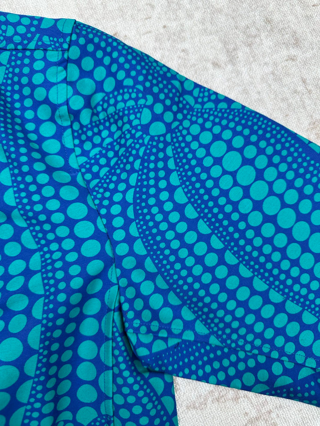 Blue long-sleeve button-up shirt with teal dot pattern on folded side