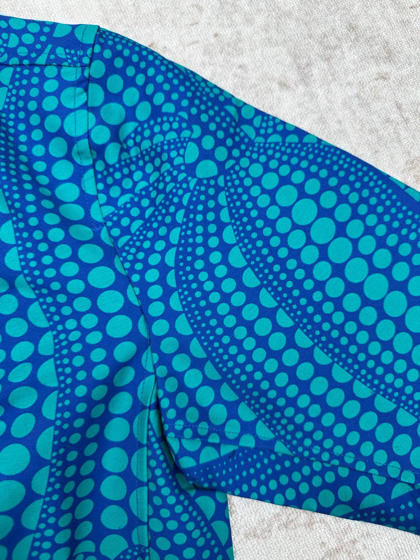 Blue long-sleeve button-up shirt with teal dot pattern on folded side