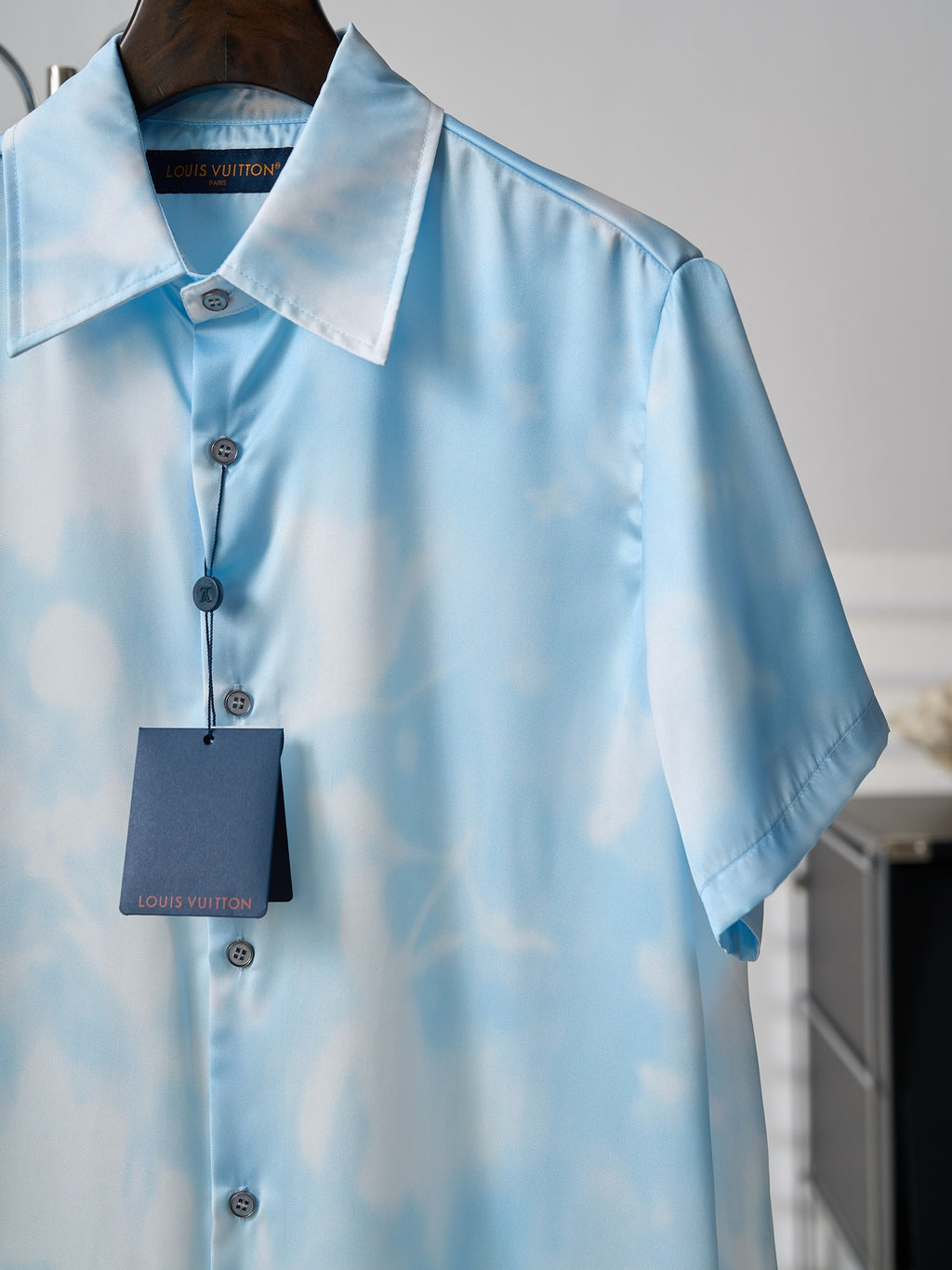 Light blue short-sleeve button-up shirt on hanger, button placket and hanging tag