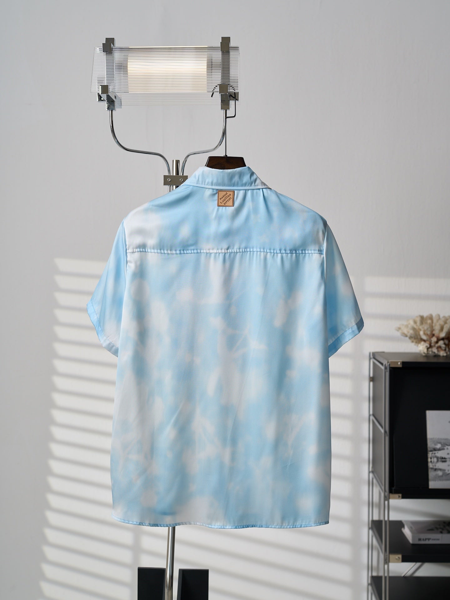 Light blue short-sleeve button-up shirt on hanger, back yoke and stitched hemline
