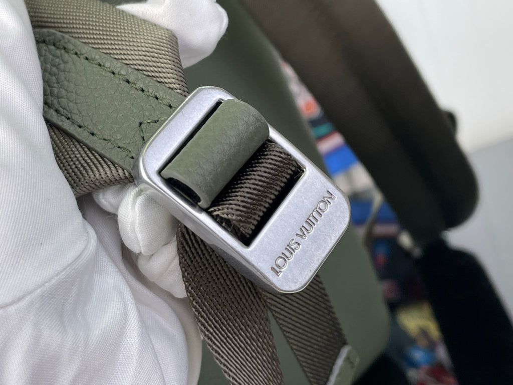 Louis Vuitton leather backpack strap buckle close-up with engraved LV mark, sage green.