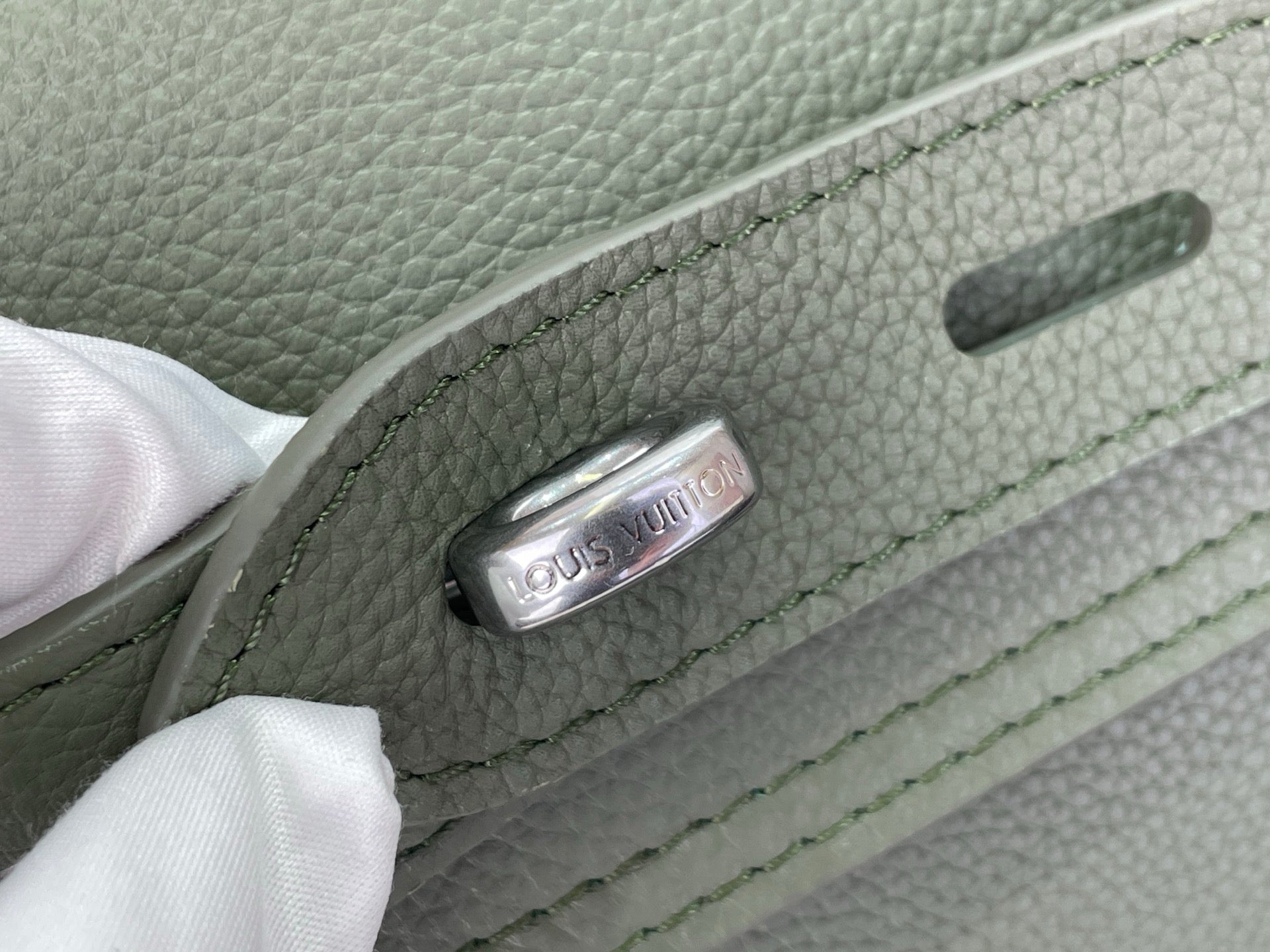 Louis Vuitton leather backpack close-up of engraved hardware on sage green strap tab.