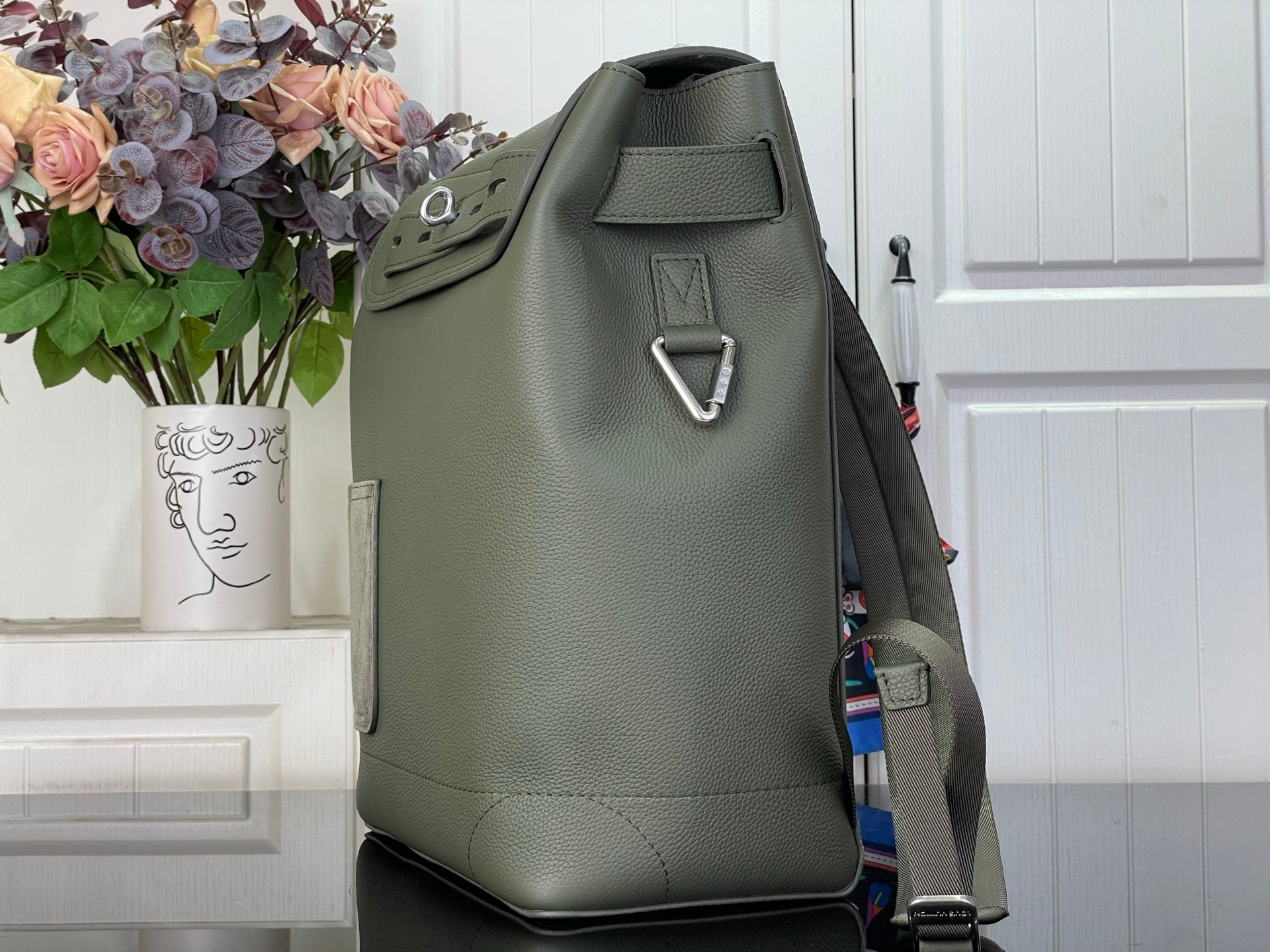 Louis Vuitton leather backpack side view with top handle and metal loop, sage green.
