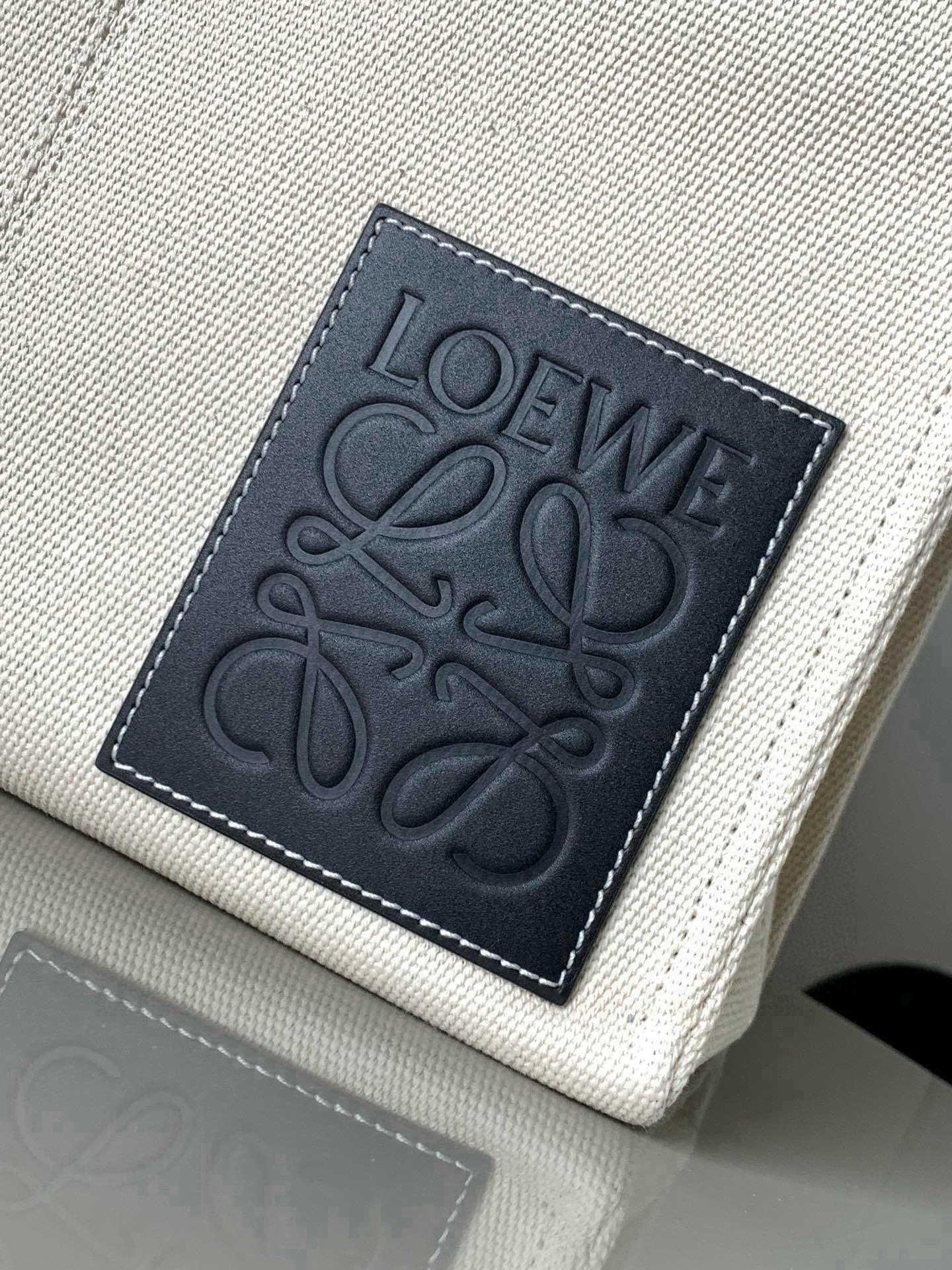 Cream canvas tote bag close-up of dark stitched front logo patch